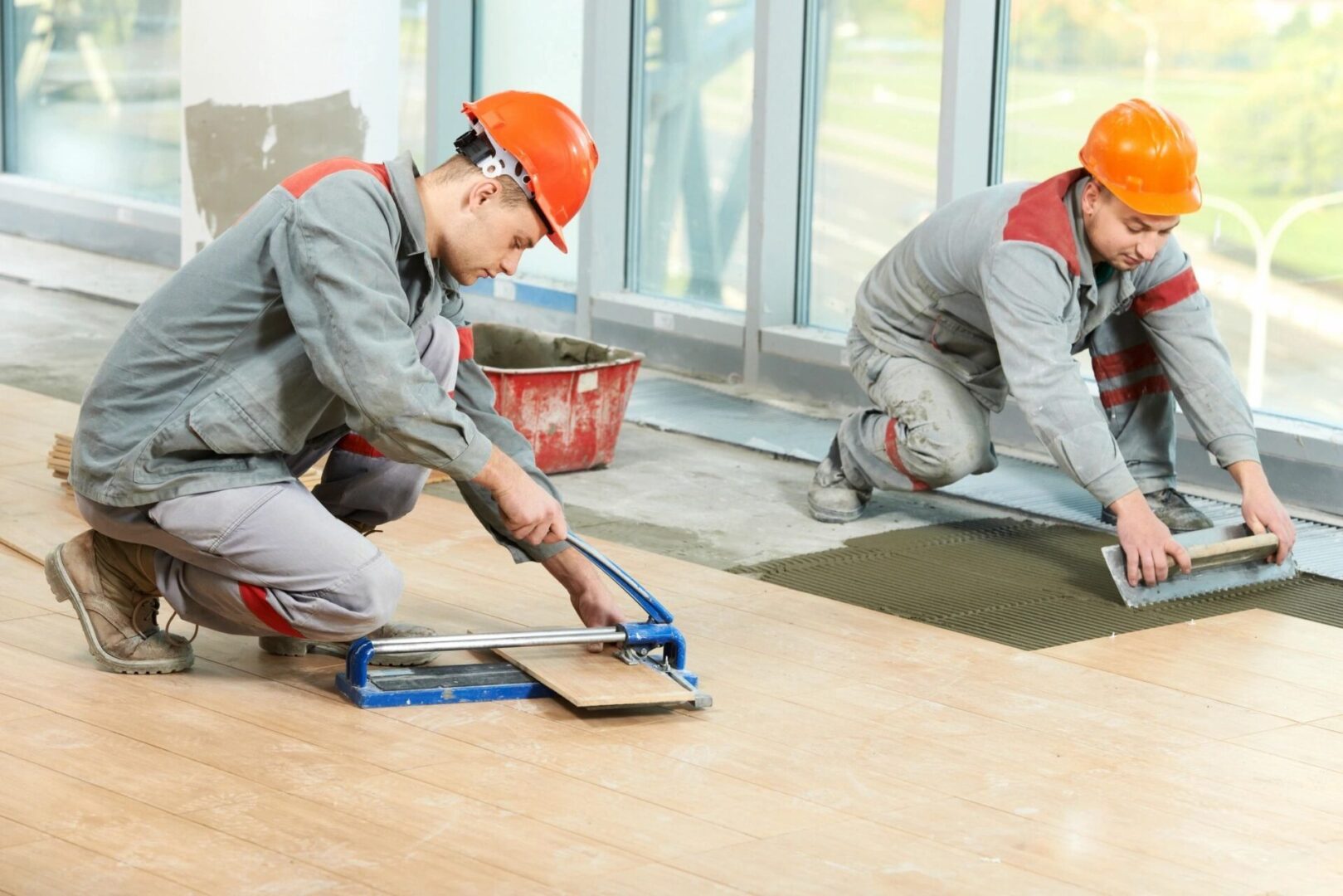 Two men in hard hats working on a floor.